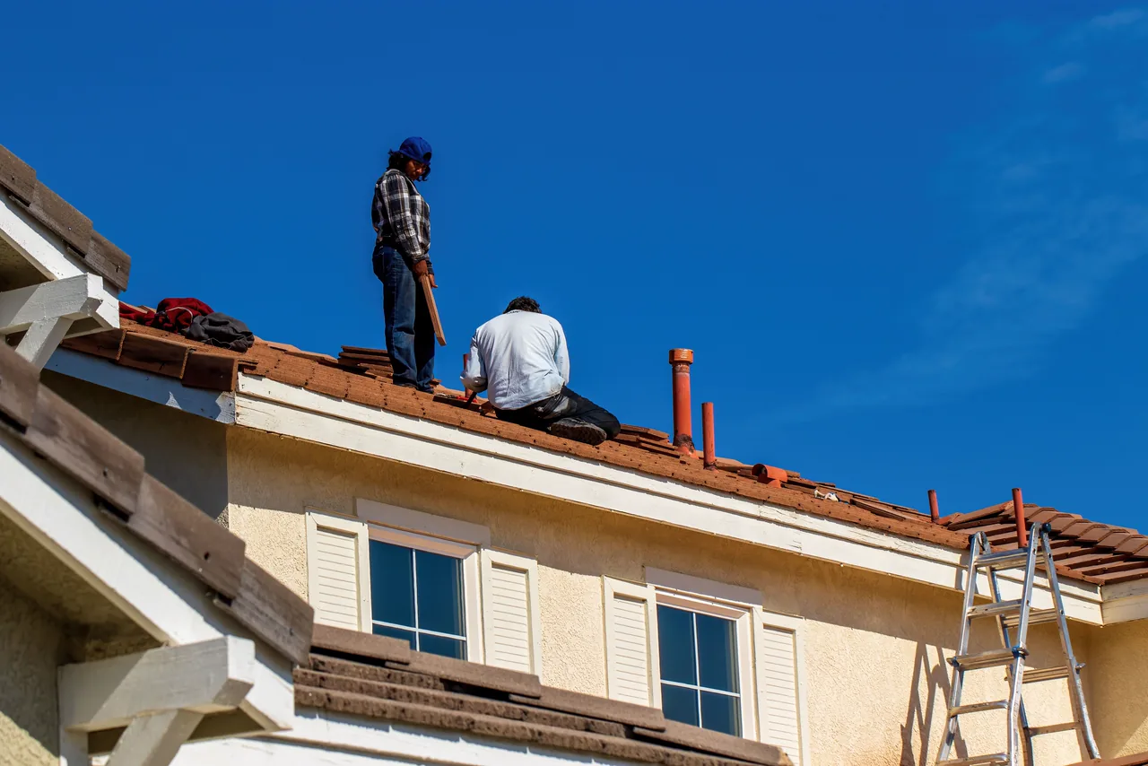 Two roofers working on a tiled roof under a blue sky